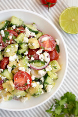 Delicious Avocado Tomato and Cucumber Salad in a bowl on cloth, top view. Flat lay, overhead, from above. Close-up.