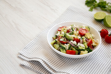 Delicious Avocado Tomato and Cucumber Salad in a bowl on a white wooden background, side view. Copy space.