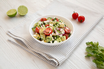 Delicious Avocado Tomato and Cucumber Salad in a bowl on a white wooden background, side view.
