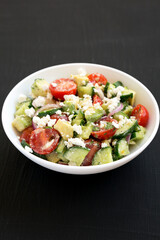 Delicious Avocado Tomato and Cucumber Salad in a white bowl on a black surface, low angle view.