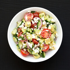 Delicious Avocado Tomato and Cucumber Salad in a white bowl on a black surface, top view. Flat lay, overhead, from above.