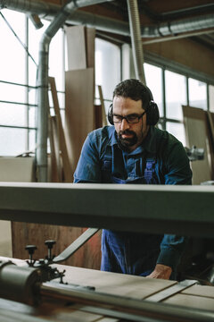 portrait of a bearded woodworker with black protection earmuffs working on a belt sander