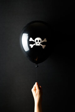 Hand holding black balloon with skull