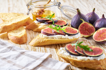 bruschetta with ricotta cheese, fresh figs, honey and arugula on a wooden table.