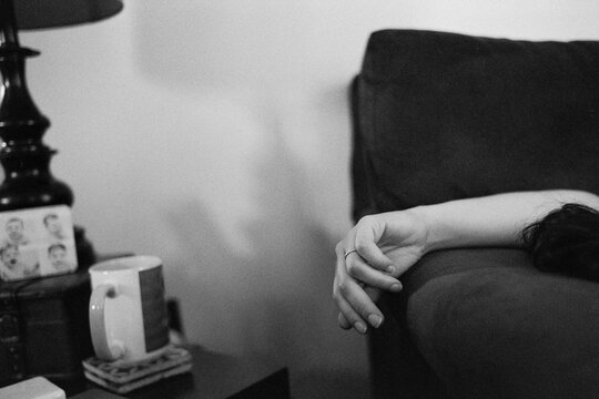 The hand of a woman hangs over the armrest of a sofa as she naps on a lazy Sunday afternoon