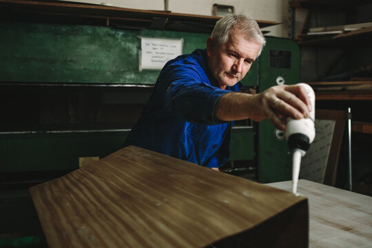 portrait of male senior woodworker applying glue on wooden veneer - Powered by Adobe