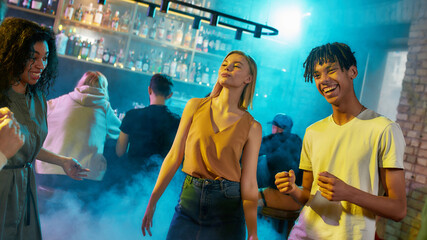 Attractive caucasian young woman and mixed race guy having fun, dancing with friends at party in the bar