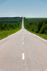 Empty country road on a summer day with green plantings of forest and greenery on the sides