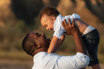 Happy African American father and son having fun outdoors. Dad and son playing on the beach at the sunset time