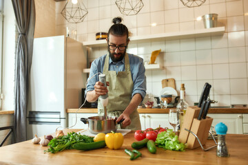 Young man, chef cook using hand blender while preparing Italian meal in the kitchen