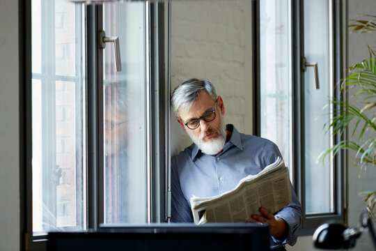 Businessman Reading Newspaper By Window In Office
