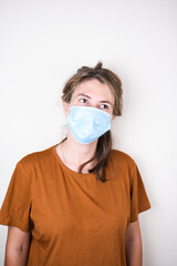 young woman in a medical mask and home clothes looks at the camera isolated on a colored...