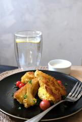 Roasted cauliflower with tomato cherries and fresh parsley on the black plate with a glass of water