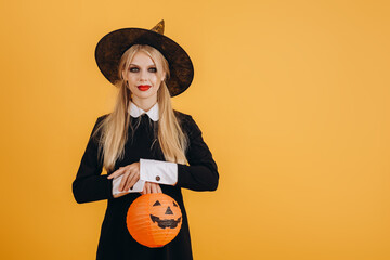 Cute halloween girl holding a painted orange lettering on an orange wall background