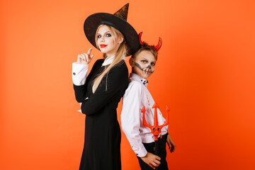 Halloween boy and girl stand back to back on orange wall background