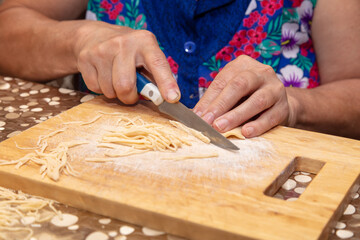 A woman cuts noodles from dough