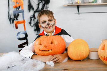 Cute boy dressed as Dracula at a party on Halloween holding a pumpkin on a background of scenery