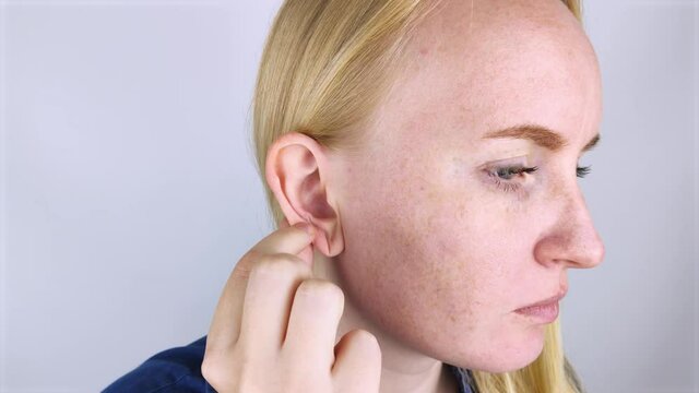 A woman on a white background shows her ear. The macro video shows the curl of the auricle, which has a tubercle. Plastic surgery concept