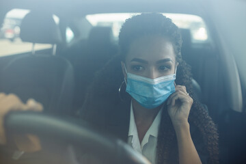Young business woman adjusts her medical mask and stay safe while driving her car during covid-19 pandemic. Business trips during pandemic, new normal and coronavirus travel safety concept.