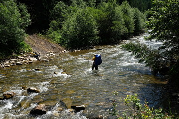 Hiker man hiking crossing river. Trekking journey and travel concept