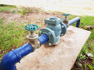 Fototapeta na wymiar Industrial water meter with valve. With blue metal pipes for delivering water to office buildings or large buildings On the background, cement base and earthen patio. Selective focus