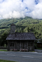 Fototapeta na wymiar Wooden chapelle by the road with forest hills in background