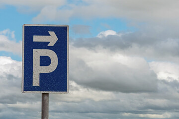 Blue and white parking sign with direction to the right arrow,  cloudy sky in the background.