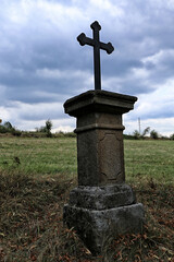 Fototapeta na wymiar Old metal crucifix on stony pedestal on the grassy hillside