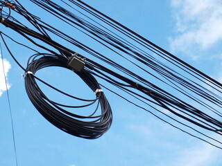 Electric wires roll on the cable. There is a low voltage line above it on a blue sky background with white clouds with a copy area. Focus closely and choose the subject.