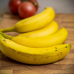 von vorne nach hinten fotografierte gelbe Bananen mit Schärfeverlauf und Tomaten im Hintergrund