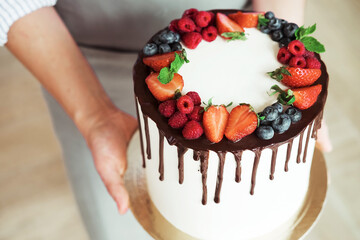Young smiling brunette woman chef holding a homemade cake decorated with chocolate and fresh...