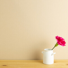 Vase of pink carnation flower on wooden table with beige background