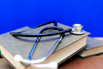Stethoscope with stack of books on table or blue background.Medical literature concept