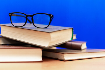 Books and eyeglasses on a wooden table, on blue soft background