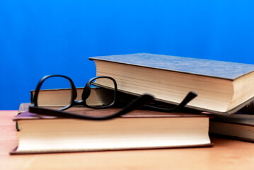 Books and eyeglasses on a wooden table, on blue soft background