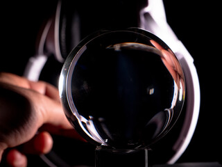 hand with a cannabis cigar and white headphones playing with its reflection in a crystal ball on a black background . Music and cannabis concept