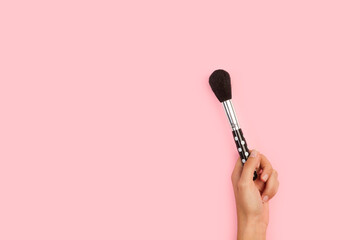 Mano femenina sosteniendo un pincel de maquillaje brocha profesional sobre un fondo rosa pastel liso y aislado. Vista de frentey de cerca. Copy space. Concepto: Belleza