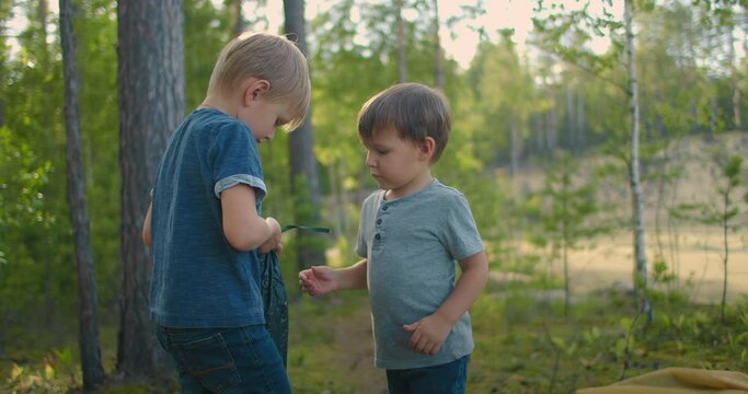 Two little boys in the woods helps to lay out and set up a tent in slow motion
