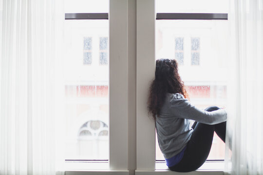 Woman sits on windowsill gazing out the window.