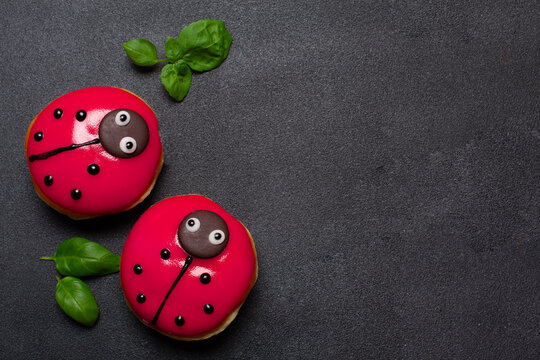 Colourful ladybug doughnuts with strawberry jam filling, children food concept. Basil leaves. Dark background copy space, flat lay. 