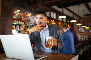 Man drinking beer and smoking cigarette while working on computer. Bad habit concept.