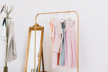 Gold floor wardrobe rack with pastel color fashion clothes near white wall. Shopping concept