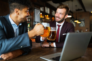 Having a pint with friend. Cheerful young men toasting with beer while sitting together at the bar