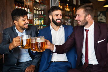 Happy young businessmen drinking beer and talking at pub after work