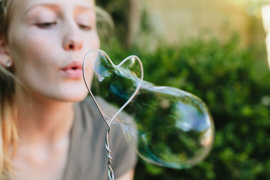 Girl Blowing Bubbles Through A Handmade Wire Heart Shaped Bubble Tool