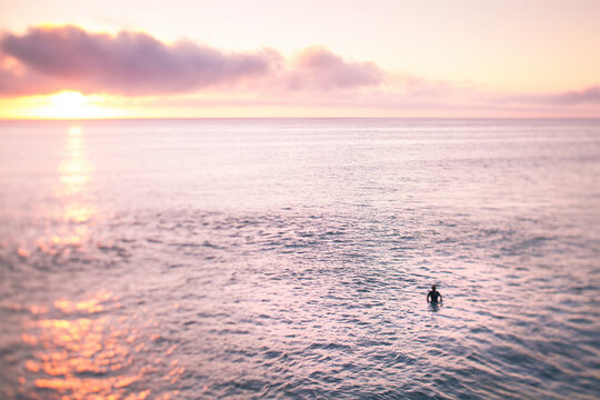 Selective focus (tilt shift) picture of a surfer at sunset.