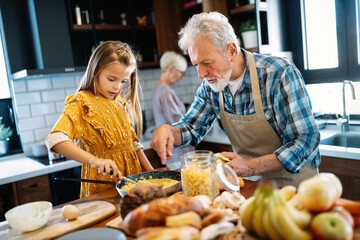 Happy young girl and her grandfather cooking together in kitchen
