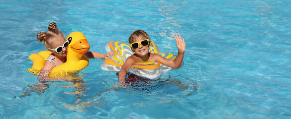 Happy children with inflatable rings in outdoor swimming pool on sunny summer day