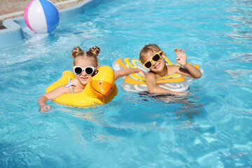 Happy children with inflatable rings in outdoor swimming pool on sunny summer day