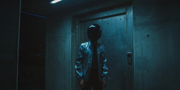 Futuristic scene with person with black helmet/mask and silver jacket with neons iluminating around.